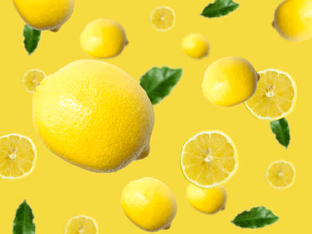 Levitation of a whole lemon and slices with green leaves on a yellow background.の写真素材