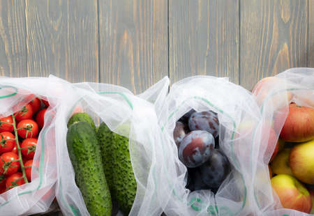 Fresh vegetables and fruits in a reusable eco-friendly pouch on a wooden background with space for your text.の写真素材