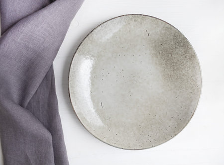 Gray linen towel and ceramic plate on a white wooden background.