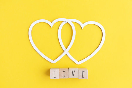 Two hearts made of white cardboard and letters with the word love on a yellow background with space for text. Postcard layout for the holiday.の写真素材