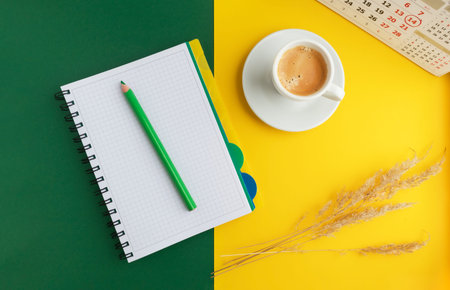 Notebook with a pencil, a cup of coffee and dried flowers on a bright yellow-green background....