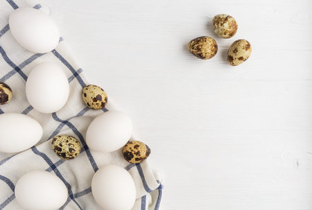 White chicken, quail eggs and a towel on a white wooden background with space for text.