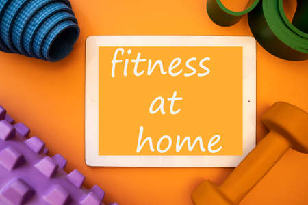 Tablet computer with sports equipment on an orange background. The concept of a healthy lifestyle in quarantine, find a home.の写真素材