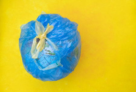 The concept of ecology and nature protection. A globe in a garbage bag on a yellow background with a place for text. Poster.の写真素材