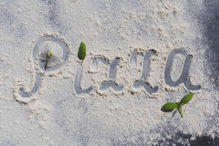 The word Pizza, written in flour on a black table with basil leaves. Menu.の写真素材