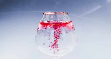 Wine glass filled with water and spreading red and yellow inkの写真素材