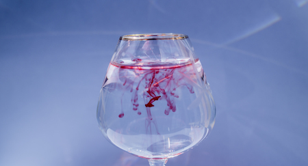 Wine glass filled with water and spreading red and yellow inkの写真素材
