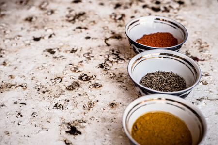 From above shot of three bowls with different spices of turmeric, cumin, and pepper on black background.の写真素材