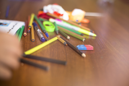 Close-up shot of assortment of colored pencils and other supplies on wooden desk.の写真素材