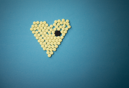 Yellow pills in shape of heart with the big black tablet on dark blue backgroundの写真素材