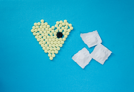 Yellow pills in shape of heart with the big black tablet on blue backgroundの写真素材