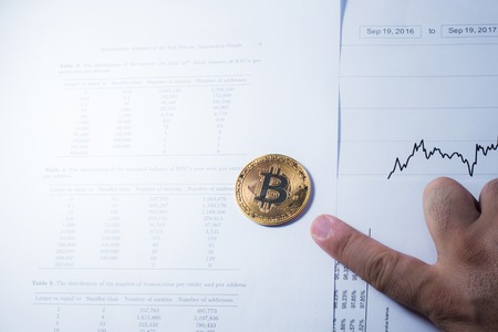Finance concept: Hand holding golden Bitcoin on charts background.の写真素材