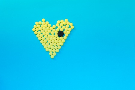 Yellow pills in shape of heart with the big black tablet on blue backgroundの写真素材