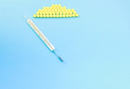 Traditional Medical thermometer and yellow pills on ligth blue background with copy space for textの写真素材