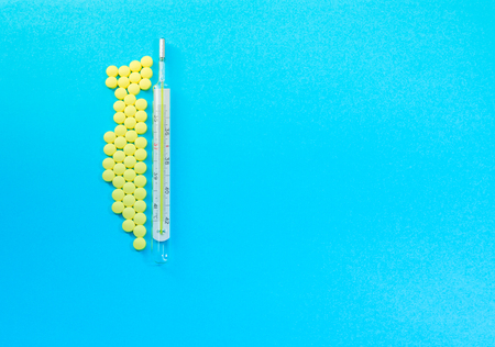 Traditional Medical thermometer and yellow pills on ligth blue background with copy space for textの写真素材