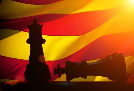 Two chess figures: one figure standing, while the second is defeated against the flag of Catalonia on background. Protests, Independence of the catalonia. A crisis. Barcelona, Spain.の写真素材