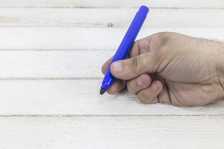 Hand holding a marker on white wooden background.の写真素材