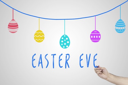 Human hand writing Easter eve against white board with drawn Easter eggs on a rope.の写真素材