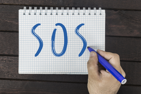 Human hand with marker writing text on notepad: SOS.の写真素材