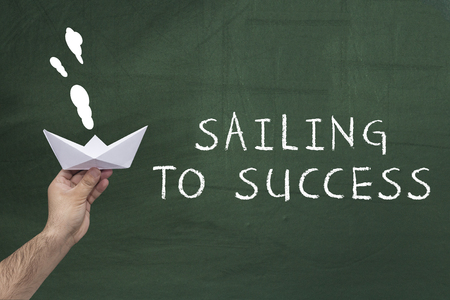 Leadership, business, success concept. Human hand holding paper boat against green blackboard with text: Sailing to successの写真素材