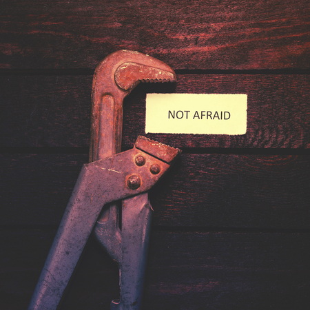 pipe wrench compresses a piece of paper with an inscription Not afraid. Toned image.の写真素材
