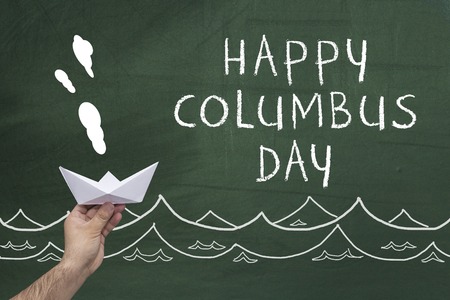 hand holding paper ship on blackboard with words: happy columbus dayの写真素材