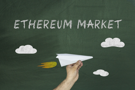 Human hand holding paper plane on the blackboard with text Ethereum market.の写真素材