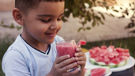 Adorable little kid boy drinking healthy fruits and vegetables juice smoothie in summer. Happy child enjoying organic drink. Blond toddler tasting watermelon juice.の写真素材