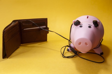 piggybank listening to wallet on yellow background. copy spaceの写真素材