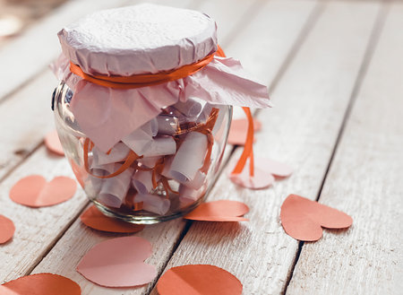 Glass jar on wood. Valentine's day concept. Date Jar with desires or wishes. Red paper hearts at background.の写真素材