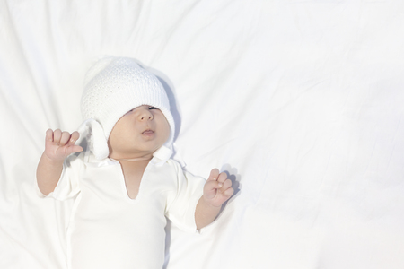 Curious little baby boy wearing white knitted hat and lying on white backgroundの写真素材