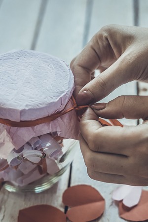 Lover's day. Hand opening glass jar or date Jar with desires or wishes. Red paper hearts at background.の写真素材