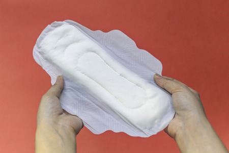 Woman's hands holding two feminine hygiene pads. Hands of female hold menstrual pads or sanitary napkins for women on pink backgroundの写真素材