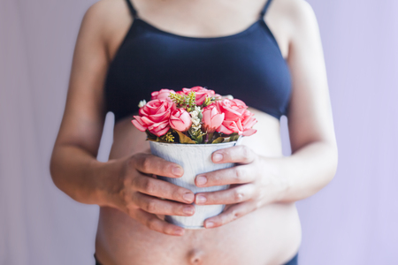 Pregnant woman holding flower pot. Pregnant woman with naked belly hold a pot of flowers in handの写真素材