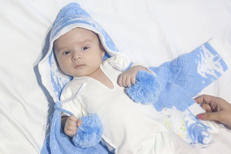 Beautiful newborn baby on white bed with white background wearing blue knitted hat or clothの写真素材