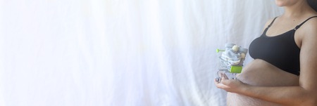 Pregnant women holding shopping cart with baby shoes. Pregnancy shopping item for children concept.の写真素材