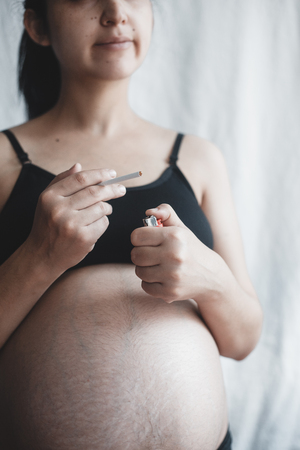 Pregnant woman smoking cigarette on bright backgroundの写真素材