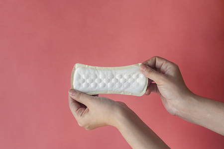 Woman's hands holding two feminine hygiene pads. Hands of female hold menstrual pads or sanitary napkins for women on pink backgroundの写真素材
