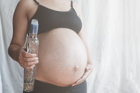 An unrecongnizable pregnant woman holding vodka bottleの写真素材
