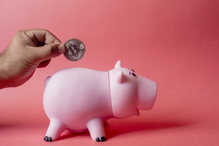 Cryptocurrency savings concept. Male hand putting bitcoin in to piggy bank. Cryptocurrency investment concept.の写真素材