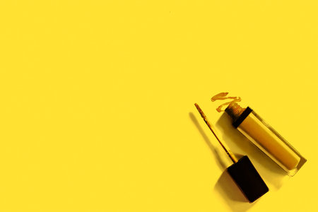 Yellow nail polish bottle with a brush on yellow background