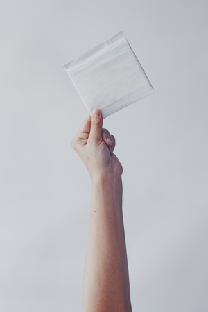 A woman put hands up holding a sanitary napkin against the white background. Period days concept showing feminine menstrual cycle.の写真素材