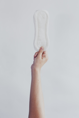 Woman hanging up sanitary pad against the white background. Period days concept showing feminine menstrual cycle.の写真素材