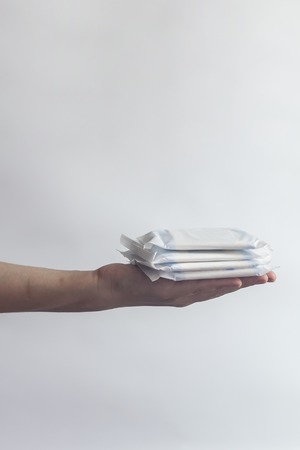 Female's hygiene products. Woman's hand holding a stack of sanitary napkins against the white background. Period days concept showing feminine menstrual cycle.の写真素材
