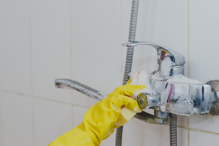 Housewife cleaning bathroom tap and shower Tap. Maid in yellow protective gloves washing dirty bath tap. Hands of woman washing or cleaning up bathの写真素材