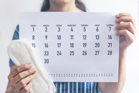 Woman holding monthly calendar and sanitary pads. Menstruation cycle calendar. Women health concept. Period days concept showing feminine menstrual cycleの写真素材