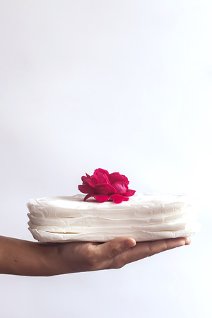 Woman's hand holding a stack of sanitary napkins with red rose on. Against the white background. Period days concept showing feminine menstrual cycle.の写真素材