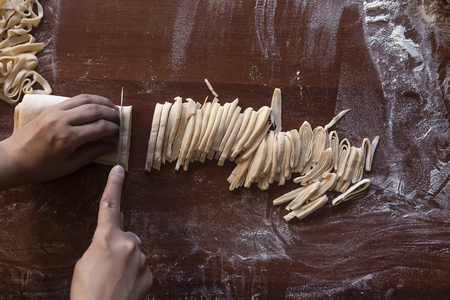 Young house wife preparing the homemade pasta at kitchen. Woman cutting long dough stripe for cooking pasta. Homemade food preparation concept.の写真素材