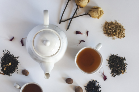 Tea set with white ceramic tea pot, dried rose flowers and other tea ingredients on the white. Flat lay view of various dried teas and teapot. View from above. Copy spaceの写真素材