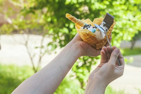 Young woman holding delicious ice cream with waffle during a picnic at nature. Summer food concept. Young adult eating yummy ice cream with a stick on a bright summer dayの写真素材